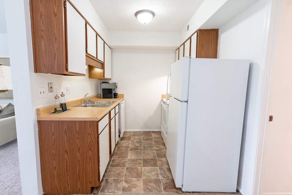 galley kitchen with white appliances and wooden cabinets at Tymberwood Trace Apartments in Louisville, KY 40219