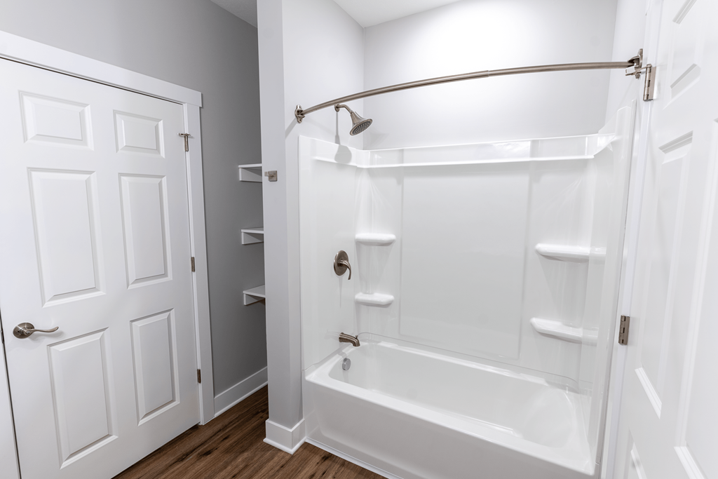 A white bathroom with a white tub and a white door.at The Village at Sandstone Apartments, Greenwood Indiana
