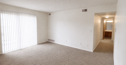 A large, empty room with carpeted flooring and a doorway leading to another room.