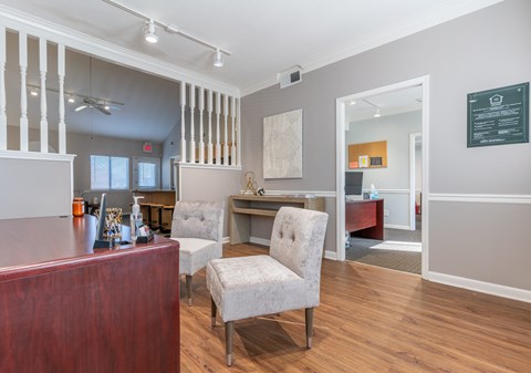 a living room with a desk and chairs and a kitchen