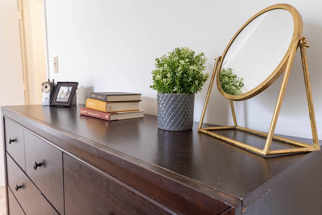 a dresser with a mirror books and a plant on it