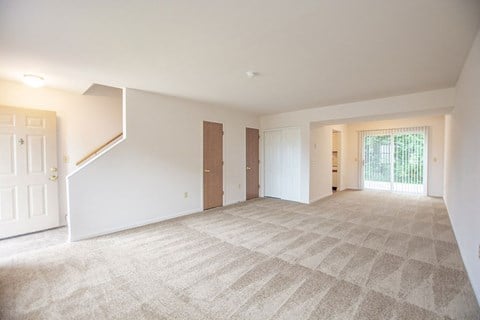 the living room and dining room of a house with white walls and carpet