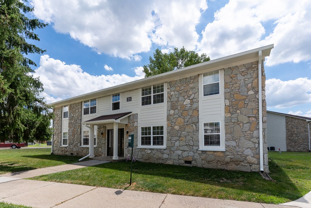 a stone and white building with a sidewalk and grass at The Court at Sandstone Apartments, Indiana