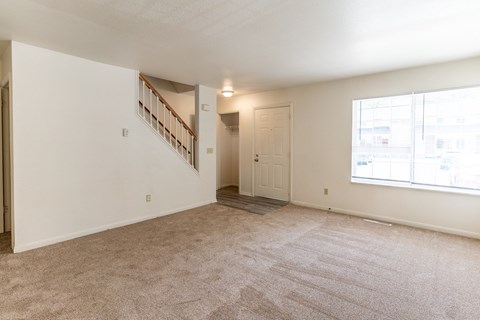 the spacious living room of an apartment with carpeted flooring and a large window