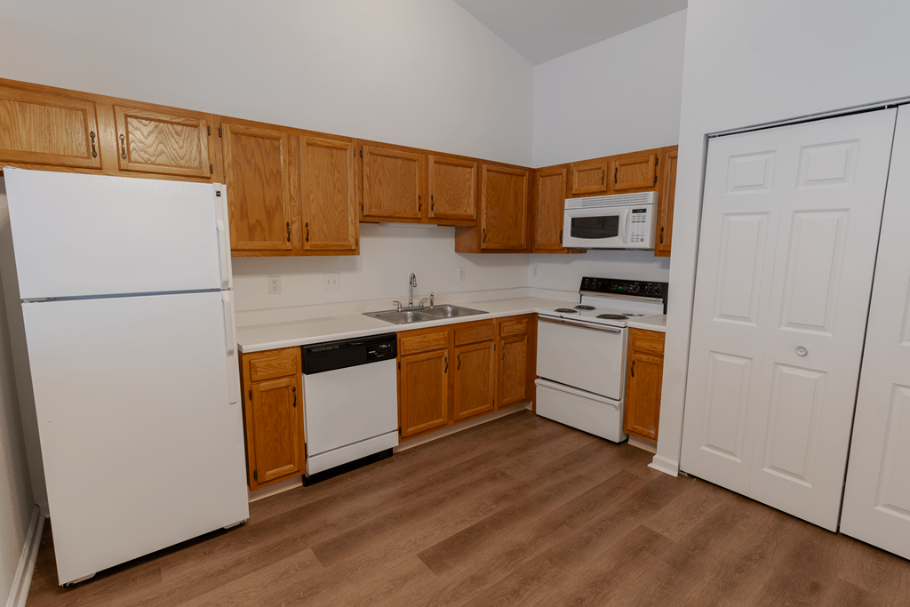 an empty kitchen with white appliances and wooden cabinets at Barton Farms in Greenwood, IN 46143