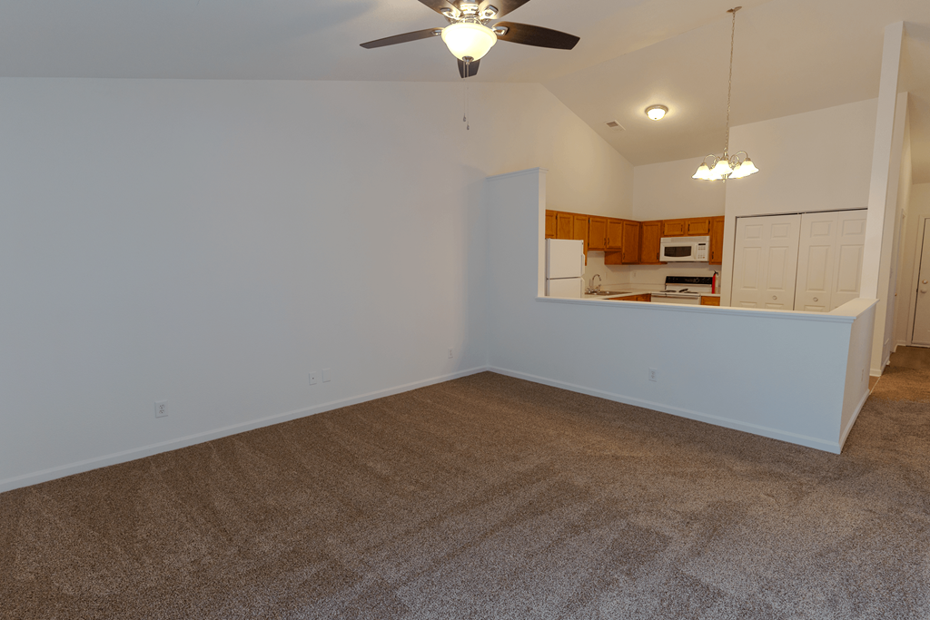 an empty living room with a ceiling fan and a kitchen at Barton Farms in Greenwood, IN 46143
