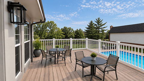 A table and chairs set on a deck with a pool in the background.