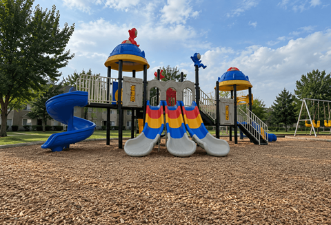 A playground with a blue slide, a yellow and blue tower, and a red and blue slide.