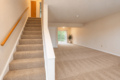 A room with a carpeted floor and a staircase with wooden handrails.