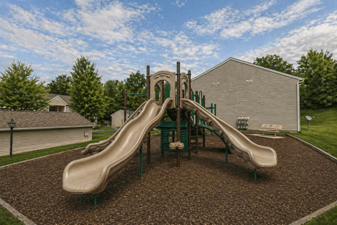 A playground with a green slide and brown ground.