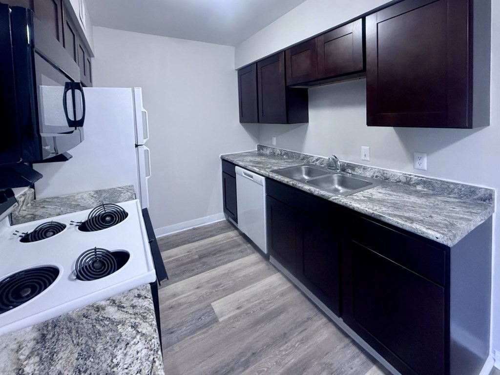 A kitchen with a white stove top oven and dark brown cabinets.