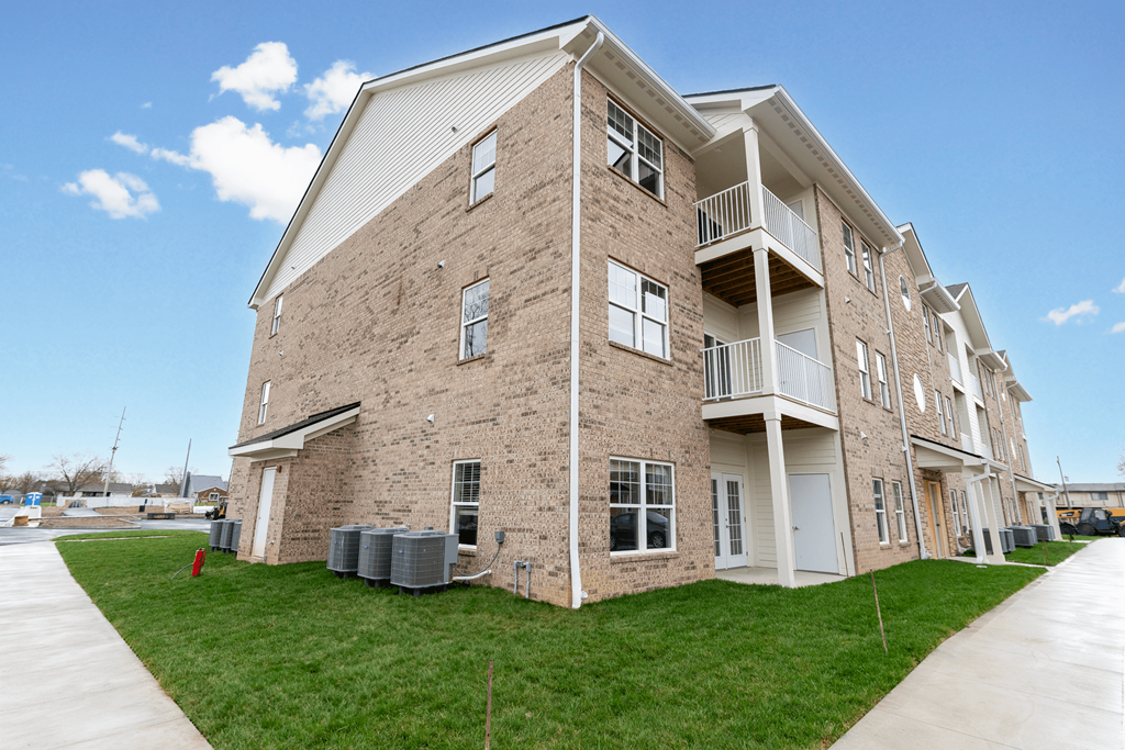 a brick apartment building with green grass and a sidewalk