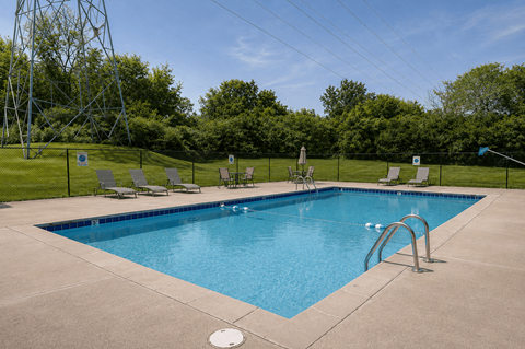A large swimming pool surrounded by a fence and lounge chairs.