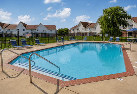 A large swimming pool surrounded by a metal fence and lounge chairs.