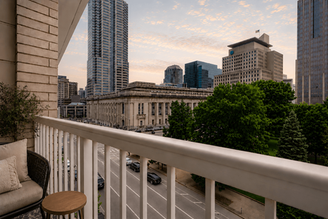 A balcony with a chair and table overlooking a city street.