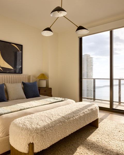 A bedroom with a large bed and a view of a cityscape through the window.