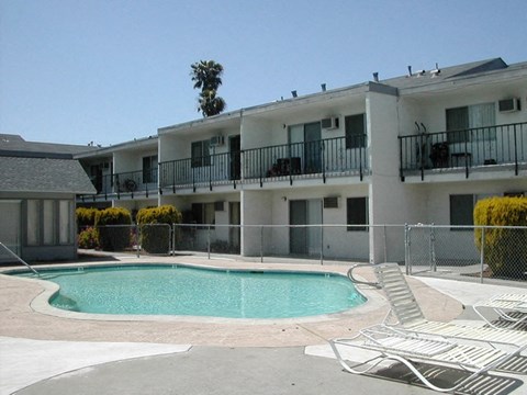 A pool surrounded by chairs and apartment buildings.