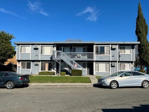 A grey apartment building with two cars parked in front.