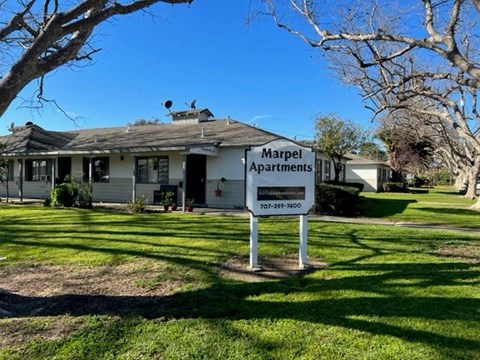 A sign for Marpel Apartments stands in a grassy area in front of a house.