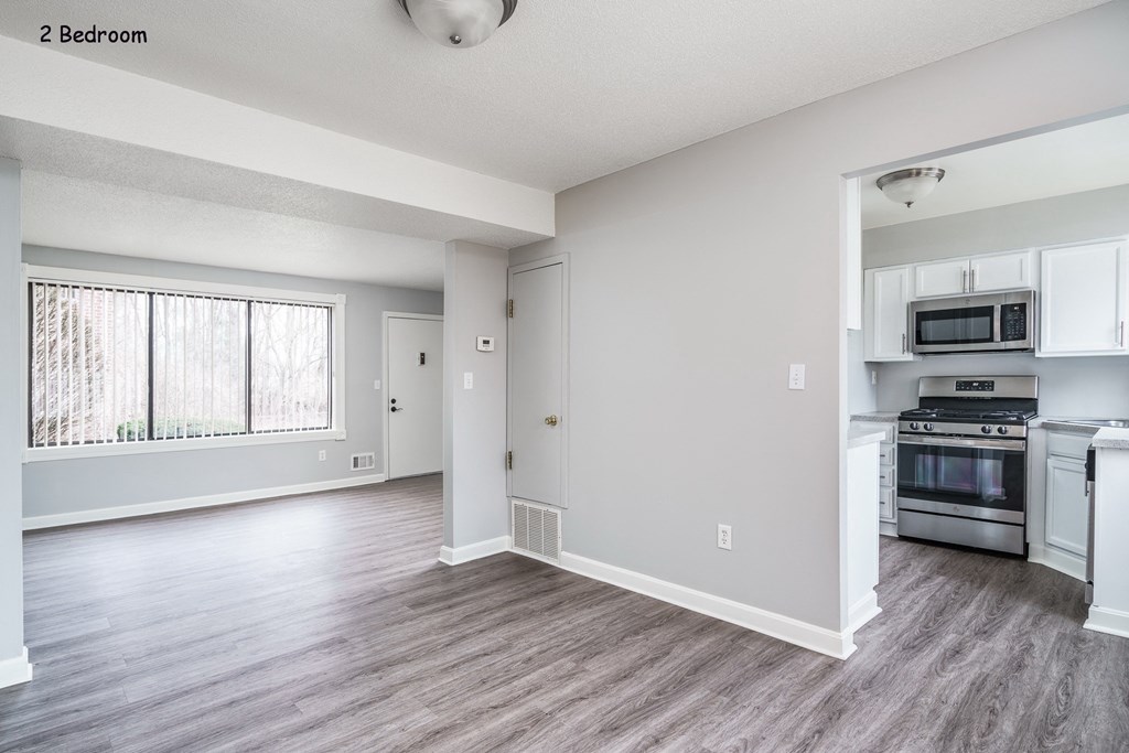 an empty living room and kitchen with white appliances and a large window