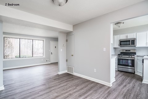 an empty living room and kitchen with white appliances and a large window