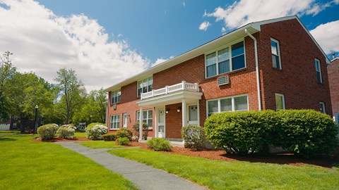 A red brick house with a white porch and green bushes in front.