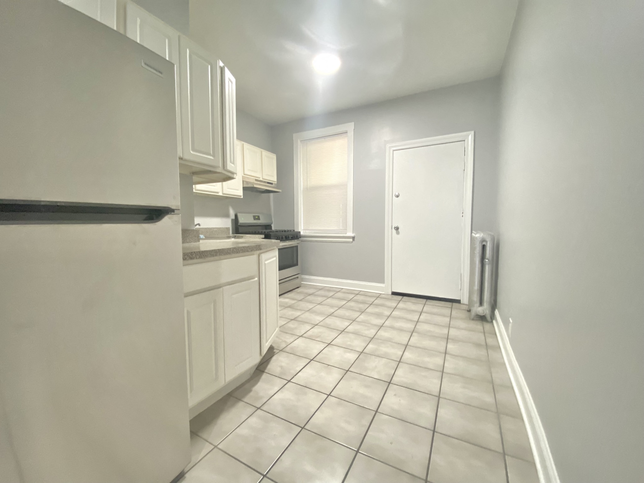 an empty kitchen with white cabinets and tiled flooring