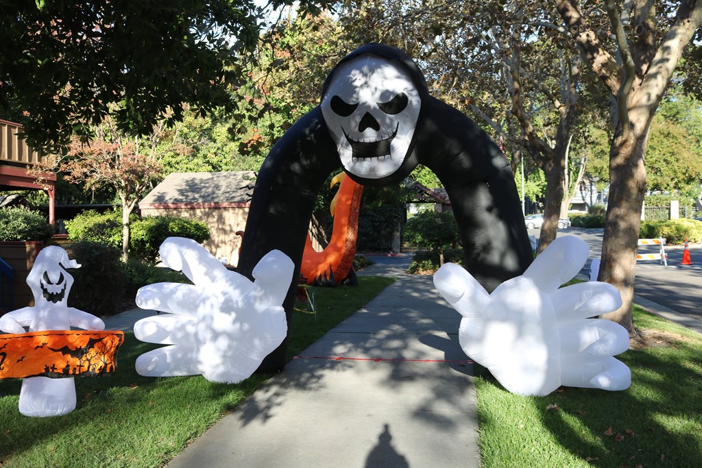 A large inflatable figure of a skeleton with a scythe is in the foreground of a Halloween-themed display.
