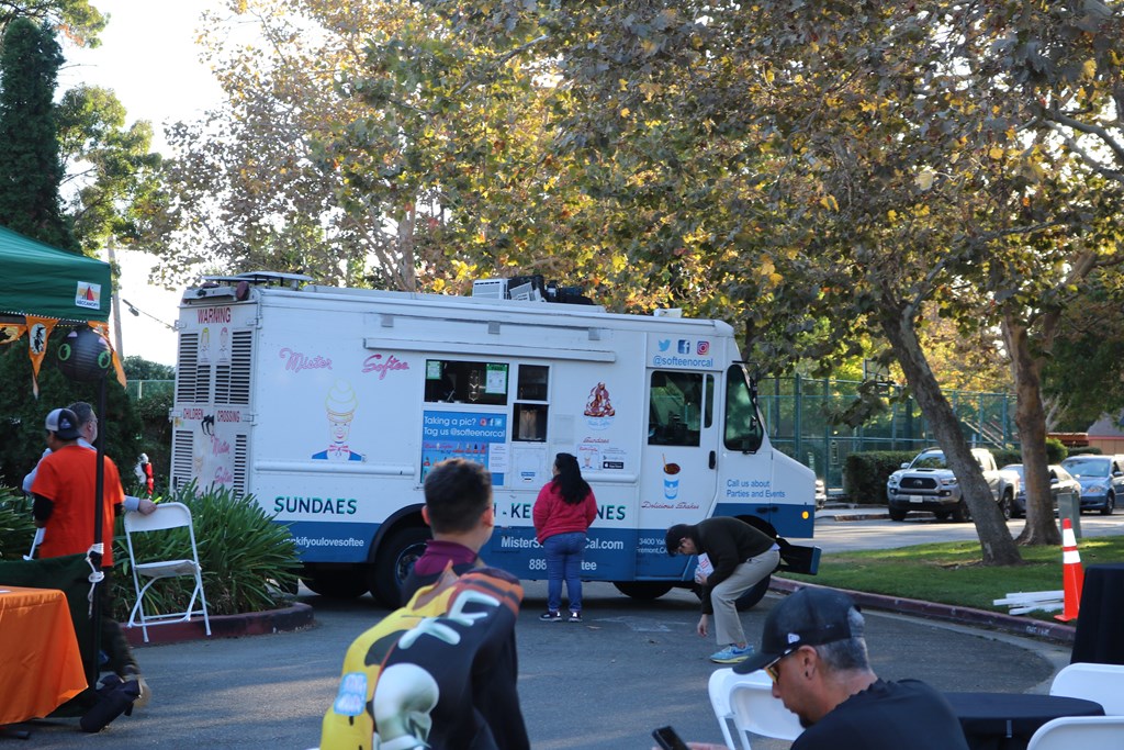 A food truck is parked on the street with people standing around it.