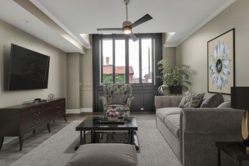 A living room with a grey couch, a coffee table, and a flat screen TV mounted on the wall.