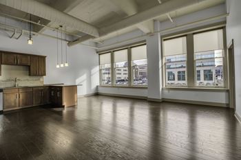 A large empty room with wooden floors and a kitchen area.