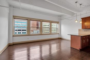 A large empty room with wooden floors and a kitchenette.