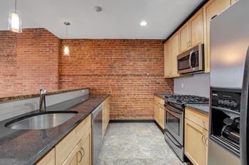 A kitchen with a brick wall and wooden cabinets.