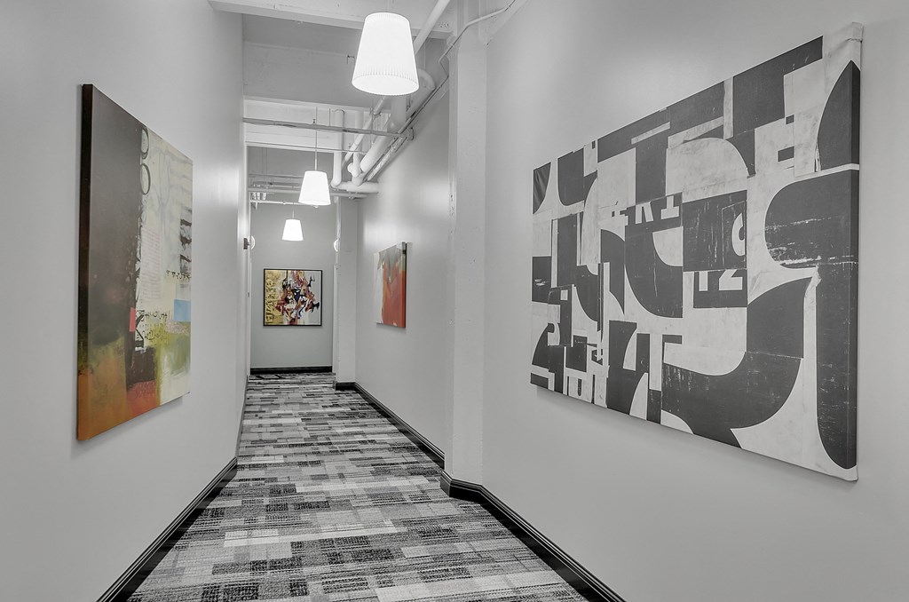 a long corridor with paintings on the wall and a hallway with a patterned carpet at 100 South Apartments, Buffalo, 14202