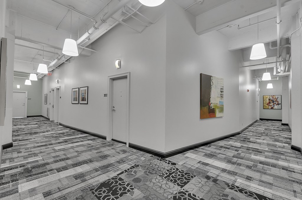 a long hallway with white walls and tiled floors and a door at 100 South Apartments, Buffalo, New York