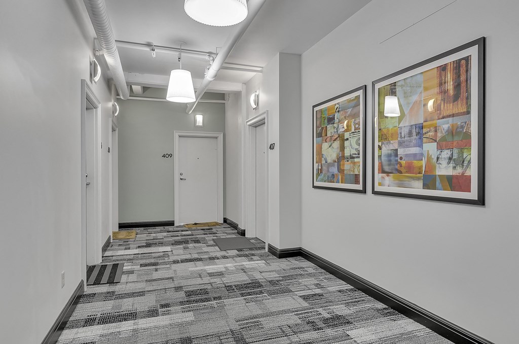 a long hallway with paintings on the wall and a door at the end of it at 100 South Apartments, Buffalo, NY