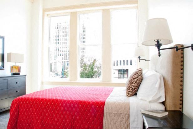 a bedroom with a red bed and three windows