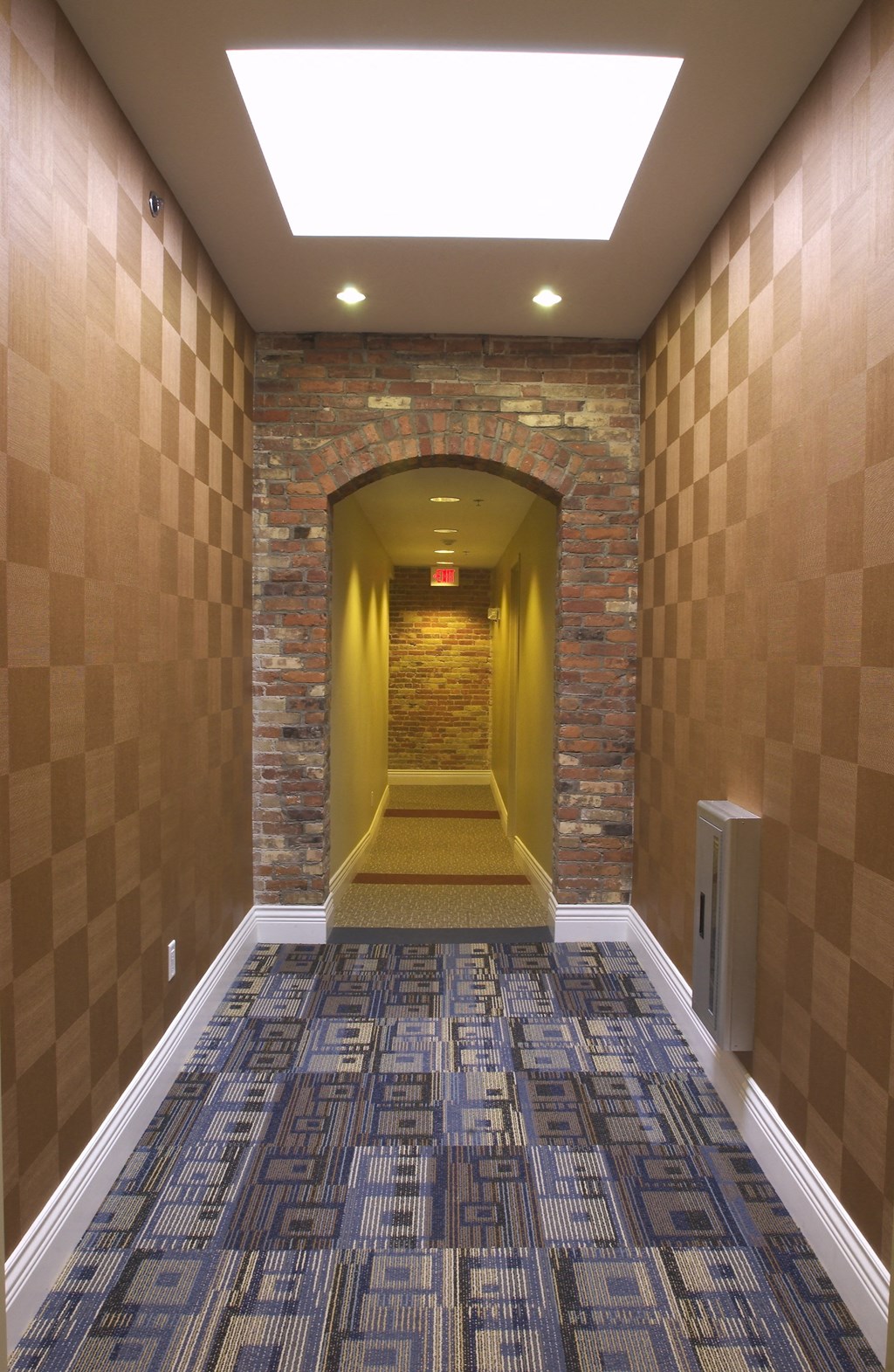 a hallway with a carpeted floor and a brick wall with a ceiling light at The Granite Works Apartments , Buffalo, New York