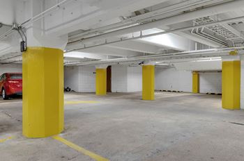 A parking garage with yellow poles and a red car in the background.