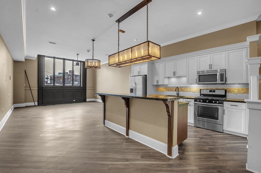 A modern kitchen with a dark wood floor and white cabinets at The Knights @ 506 Delaware Apartments, Buffalo, 14202