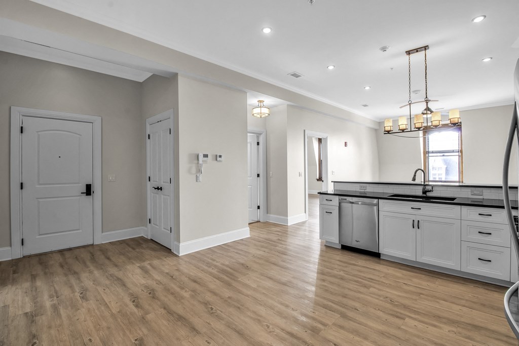 a kitchen and living room with white cabinets and a wooden floor at The Knights @ 506 Delaware Apartments, Buffalo