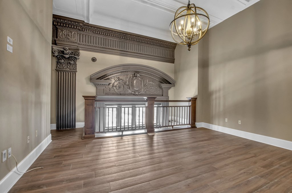 A large, empty room with a wooden floor and a chandelier hanging from the ceiling at The Knights @ 506 Delaware Apartments, New York, 14202