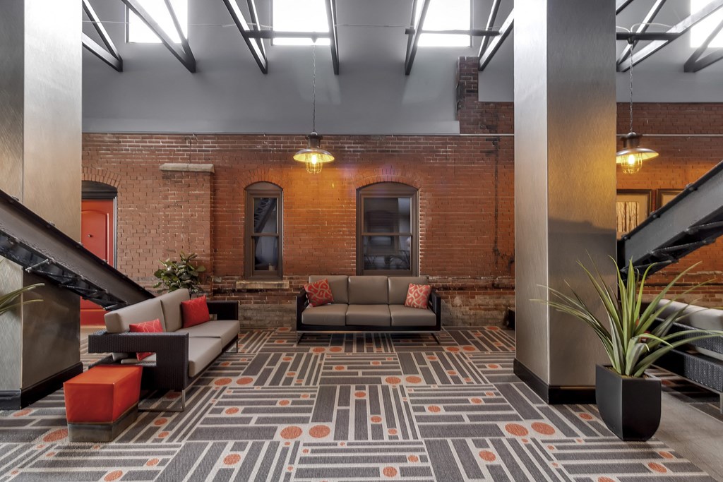 a lobby with couches and a rug in front of a brick wall at The Knights @ 506 Delaware Apartments, Buffalo, 14202
