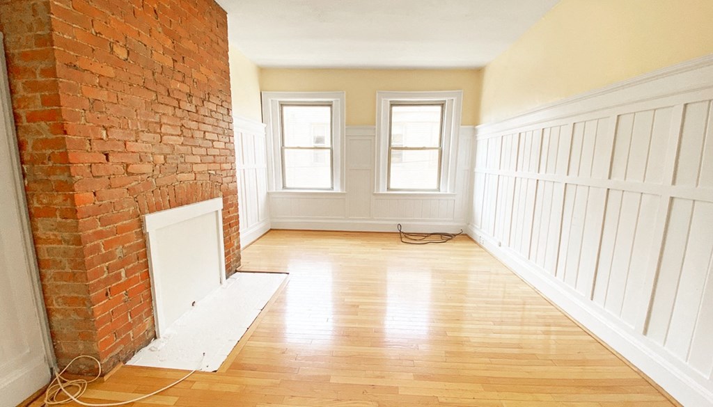 an empty room with a brick fireplace and hardwood floors
