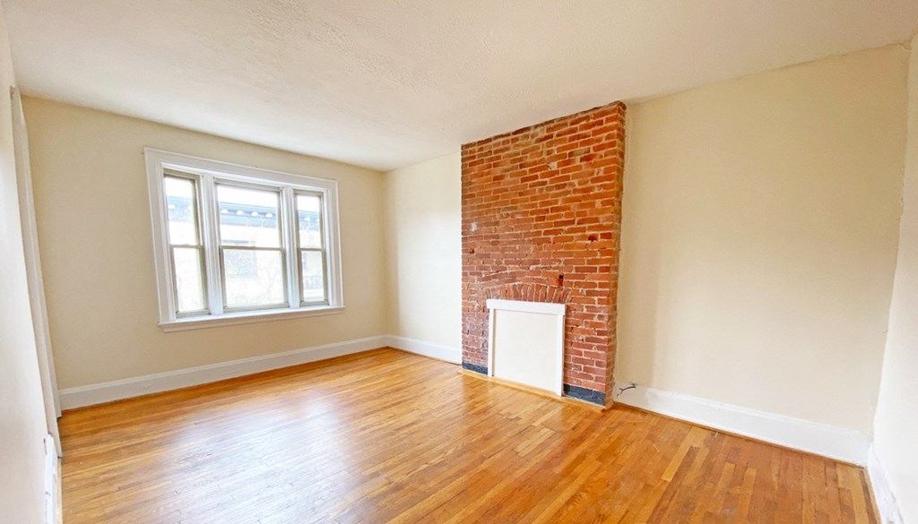 an empty living room with a brick fireplace and hardwood floors