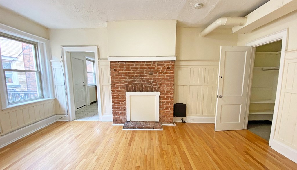 an empty living room with a brick fireplace and hardwood floors