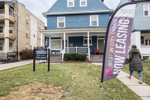 a woman walks past a blue house with a purple banner in front of it at University Commons Apartments, Oakland, Pittsburgh