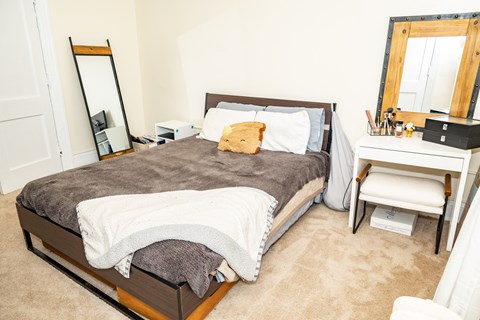 A bedroom with a bed, desk, chair, and mirror.