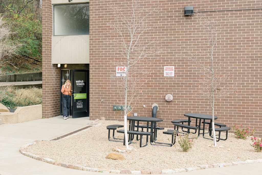A woman stands in the doorway of a brick building with a sign at Walnut Towers at Frick Park, Pittsburgh, 15217