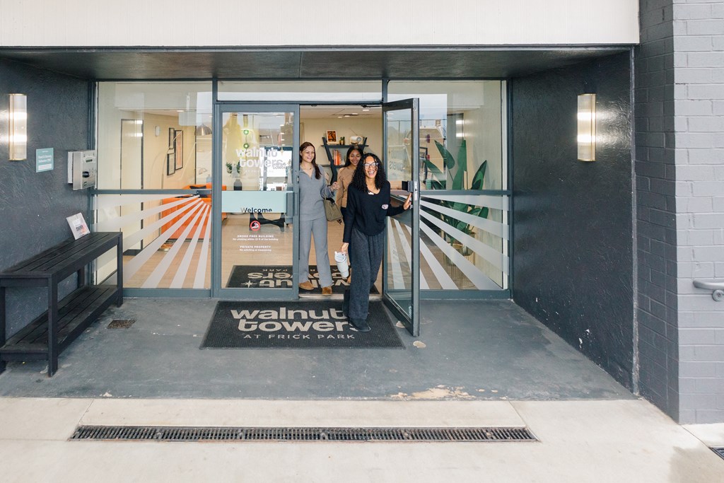 Two women standing in front of a glass door with a sign that says at Walnut Towers at Frick Park, Pittsburgh, PA 15217